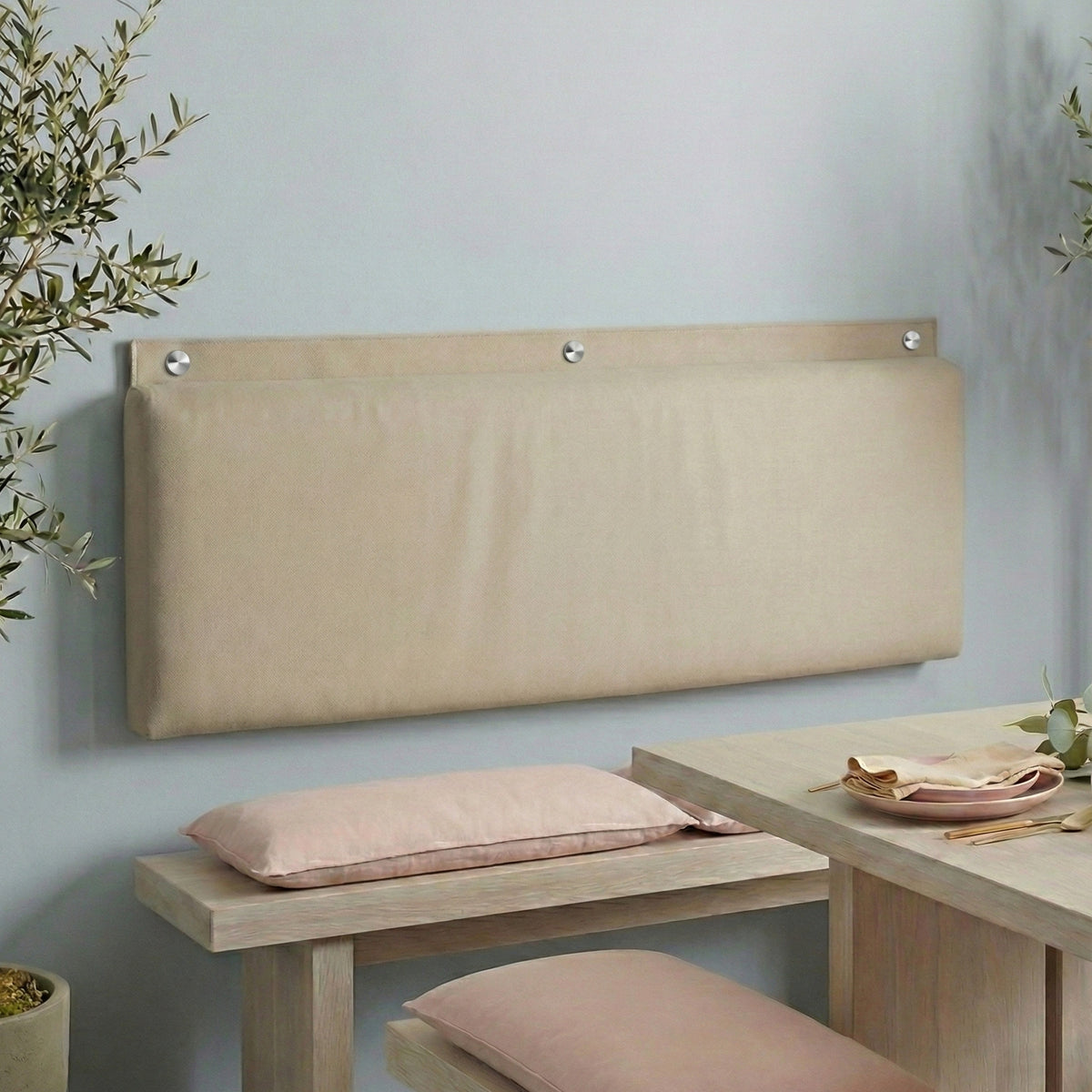 Rechteckiges, gepolstertes Wandkissen in Beige, das mit drei runden silbernen Metallkappen als bequeme Rückenlehne über einer Sitzbank oder einem Schuhregal an der Wand montiert ist, ideal für den Eingangsbereich oder das Büro.